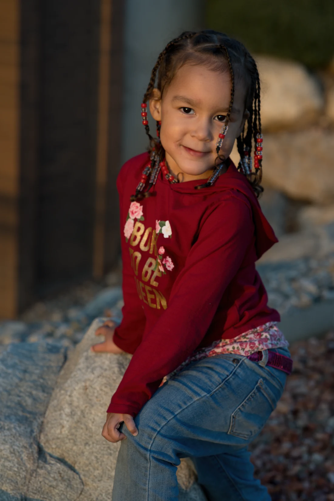 A child in a red sweatshirt sitting outdoors in warm evening light.