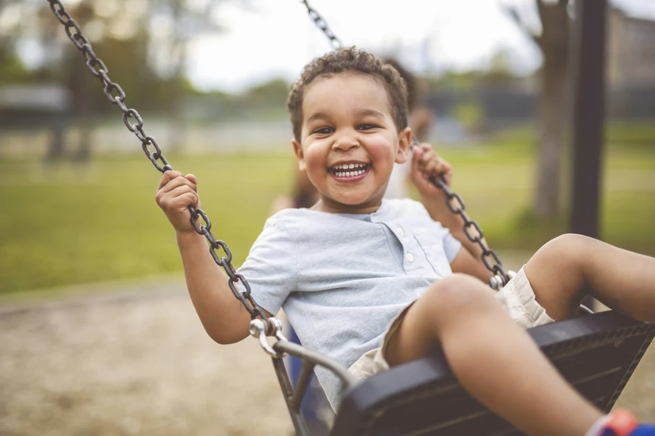 A young child laughing while riding a playground swing.