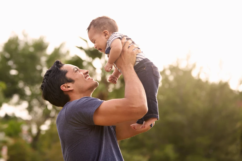 An adult lifting a smiling baby into the warm afternoon light.